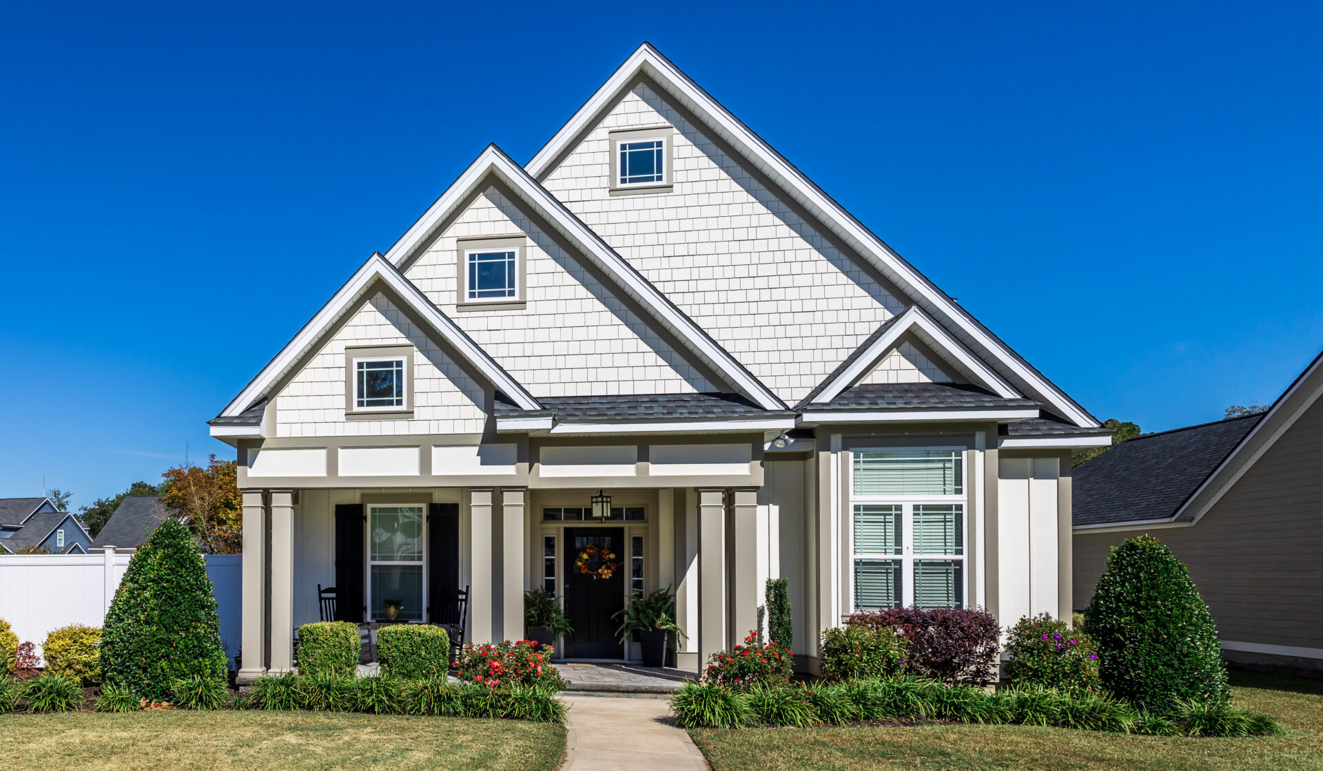 The front view of a new construction cottage craftsman style white house with a triple pitched roof with a sidewalk, landscaping and curb appeal.