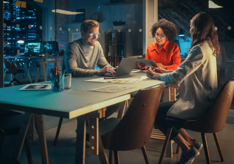 Positive Group of Managers Having a Team Meeting Long After Work Hours in the Night. Inspired Colleagues Discussing Annual Financial and Marketing Reports. Teamwork in Creative Office.