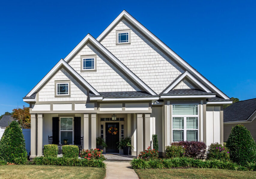 The front view of a new construction cottage craftsman style white house with a triple pitched roof with a sidewalk, landscaping and curb appeal.